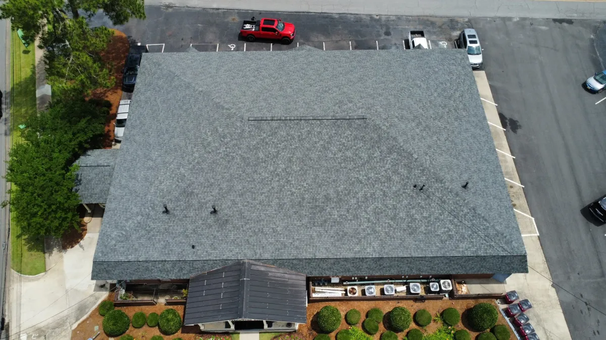 Aerial view of a finished grey architectural shingle roof on a commercial building beside its parking lot